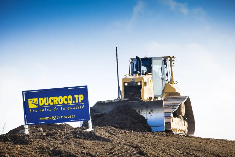 Bouteur au travail sur un chantier, devant un panneau Ducrocq TP