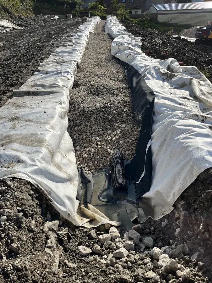Tranchée drainante en cours : géotextile, gravier et drain annelé pour les eaux pluviales