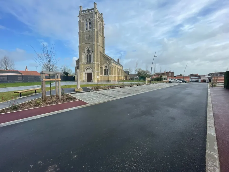 Centre-bourg réaménagé devant l'église : chaussée en enrobé noir, bande d'enrobé rouge, pavés drainants, bancs et plantations