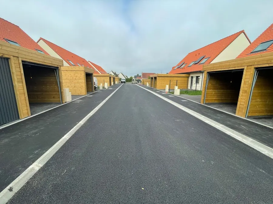Rue de lotissement en enrobé neuf et bordures, entre des garages en bois