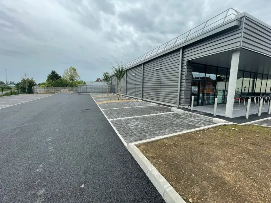 Parking de supermarché : allée en enrobé, places en pavés drainants et bordures neuves devant le magasin