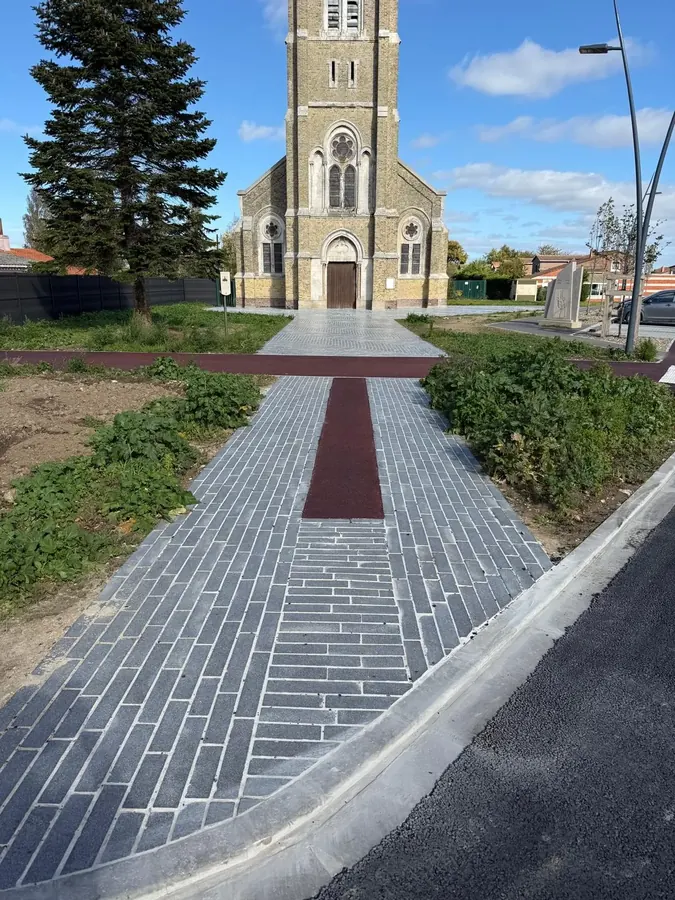 Parvis d'église en pavés gris et enrobé rouge, allée menant au portail de l'église