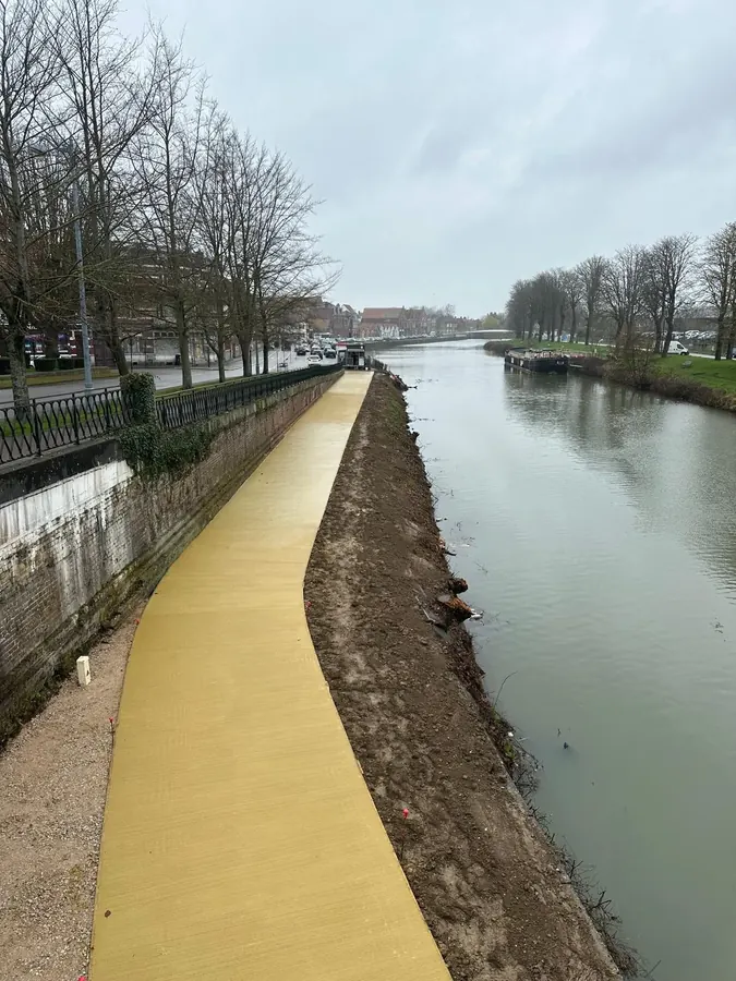 Piste cyclable en béton coloré jaune longeant un canal en centre-ville