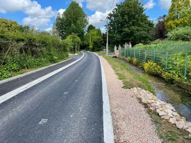 Voirie communale en enrobé neuf, bordures et accotement gravillonné le long d'un ruisseau